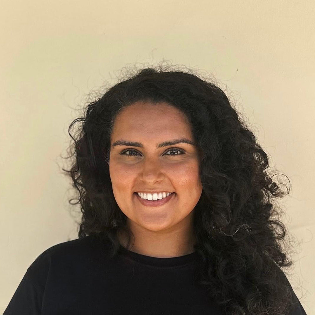 Woman with curly hair wearing a black top against a beige background